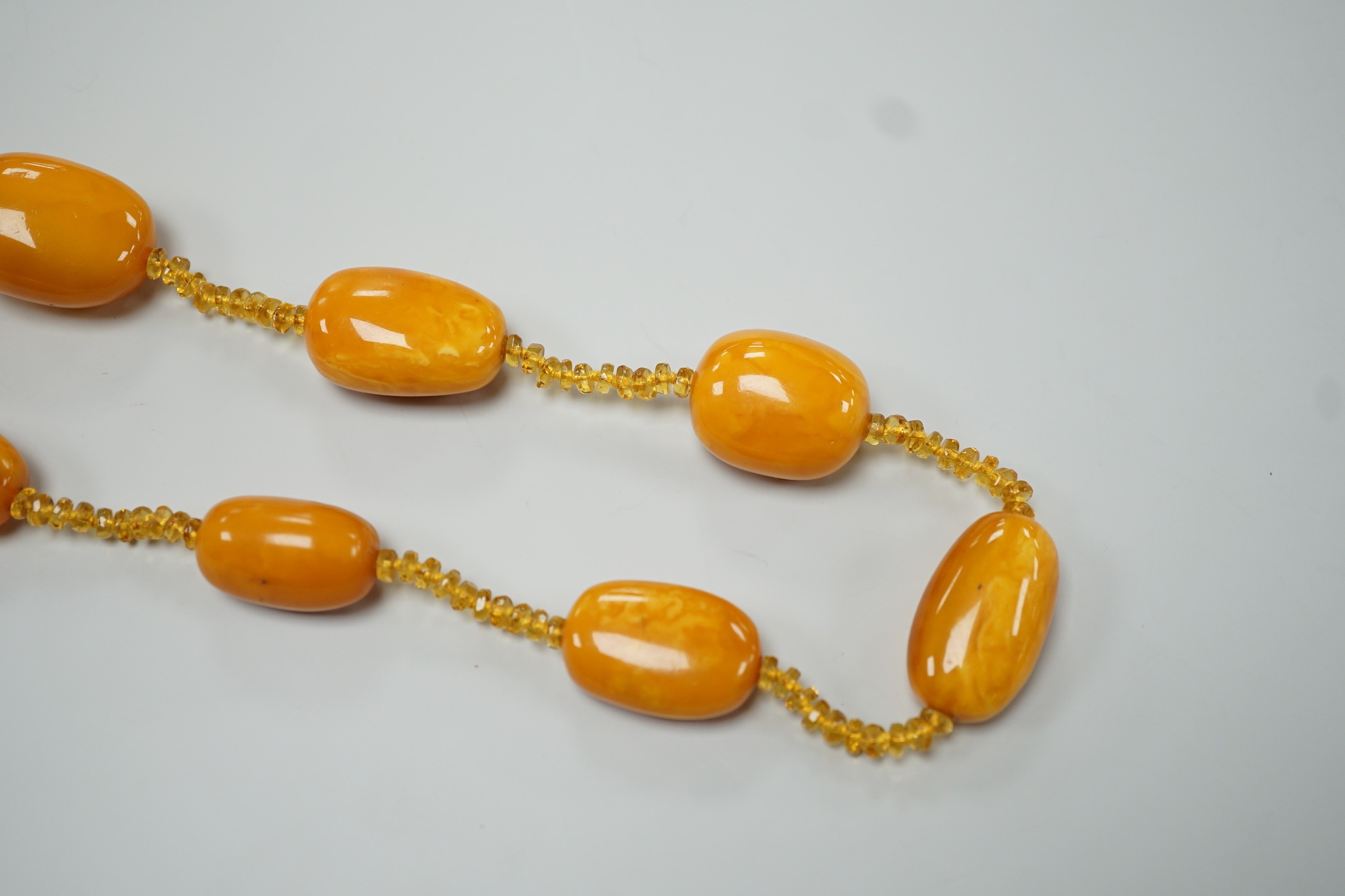 A single strand graduated fifteen amber bead necklace, with multiple amber? spacers, 84cm, gross weight 89 grams.